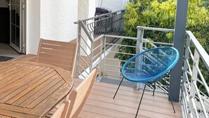 Eine Holzterrasse mit Tisch und Stühlen, ein überdachter Bereich mit Geländer und Blick ins Grüne.