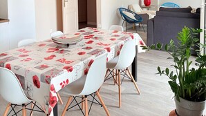 Ein Essbereich mit Tisch, bedeckt mit einer blumigen Tischdecke, weißen Stühlen und einer Pendelleuchte.
