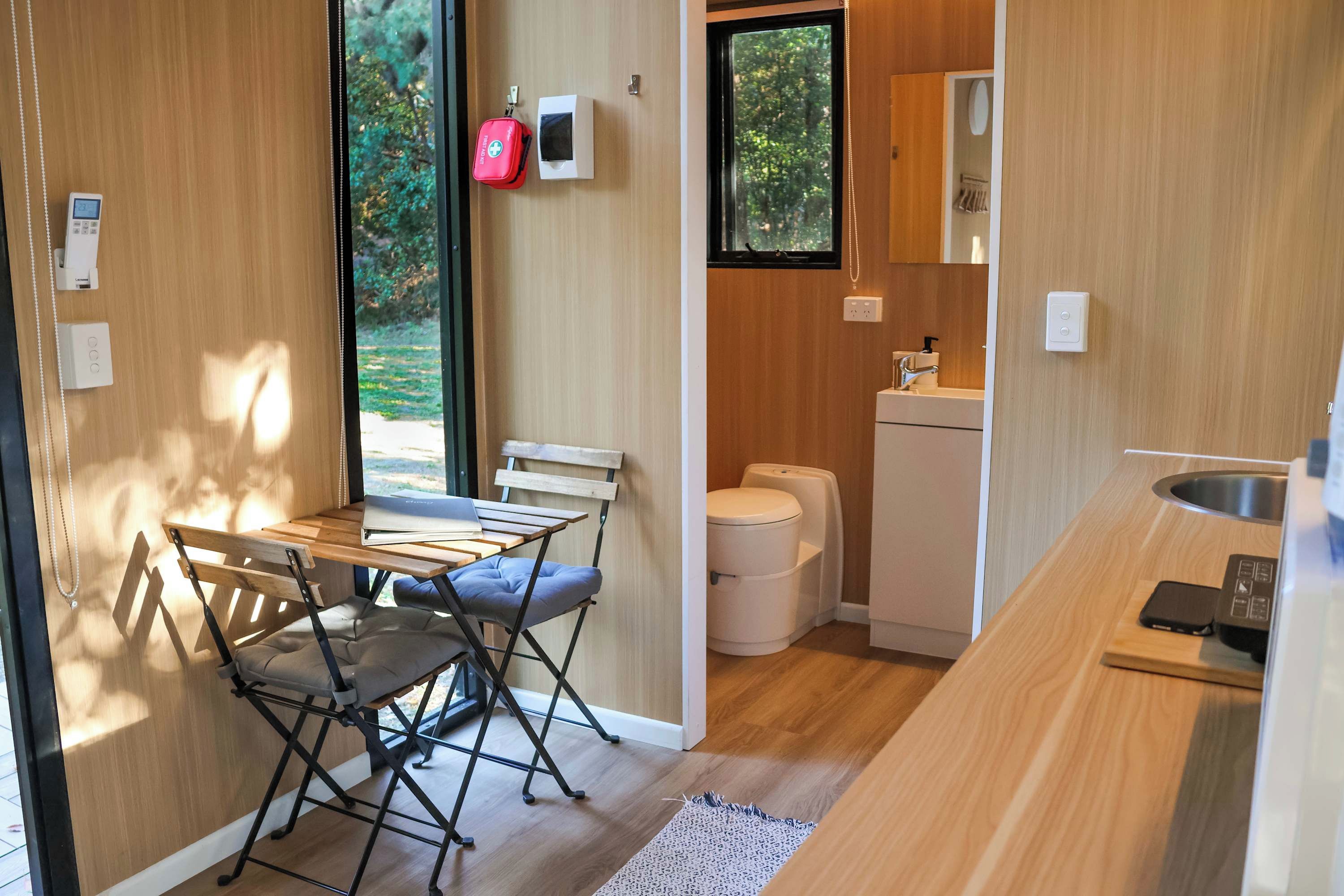 A compact kitchen with a foldable table and chairs, a sink, and a window with a view of greenery.