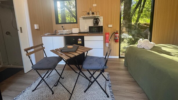 Ein gemütlicher Raum mit Küchenzeile, einem Essbereich mit Tisch und Stühlen, einem Bett mit grüner Decke und einem Fenster mit Blick auf Bäume.