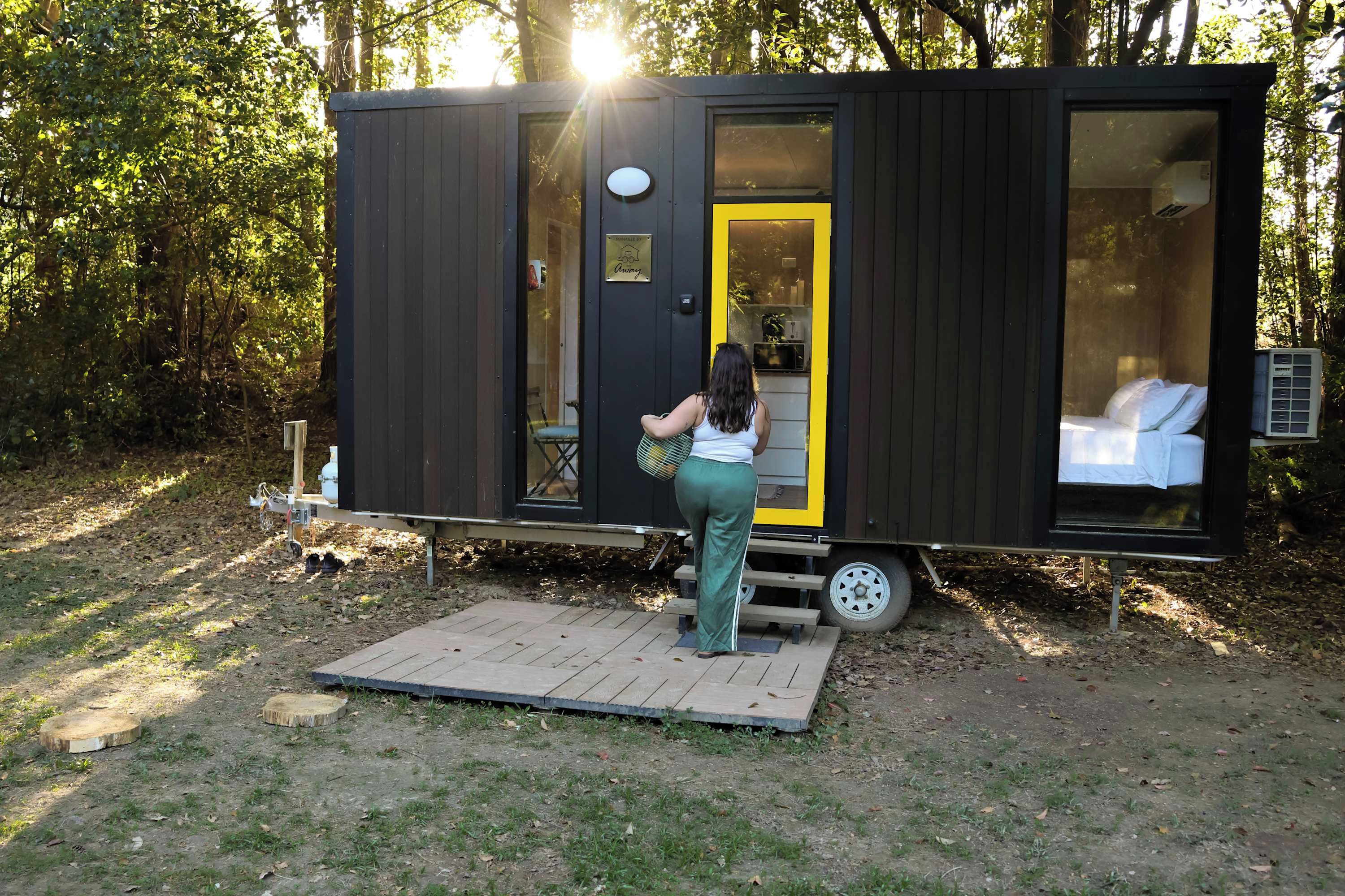 A compact, modern mobile home with a small deck area, a single visible window, and a door with a bright interior.