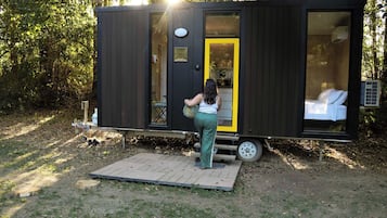 A compact, modern mobile home with a small deck area, a single visible window, and a door with a bright interior.