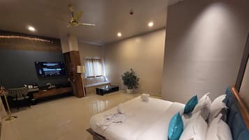 A modern hotel room with a large bed, a TV, a seating area, and a ceiling fan.