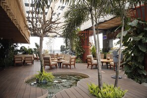 Un patio al aire libre con suelo de madera, arreglos de asientos, un pequeño estanque y plantas en macetas.
