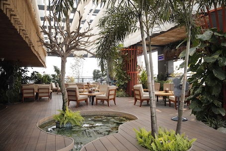 An outdoor patio with wooden flooring, seating arrangements, a small pond, and potted plants.. Hotel Subansiri