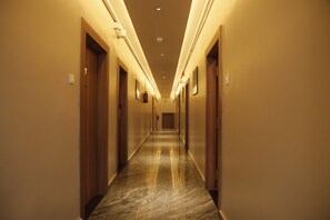 Pasillo de hotel con puertas de madera, suelo de mármol e iluminación en el techo.