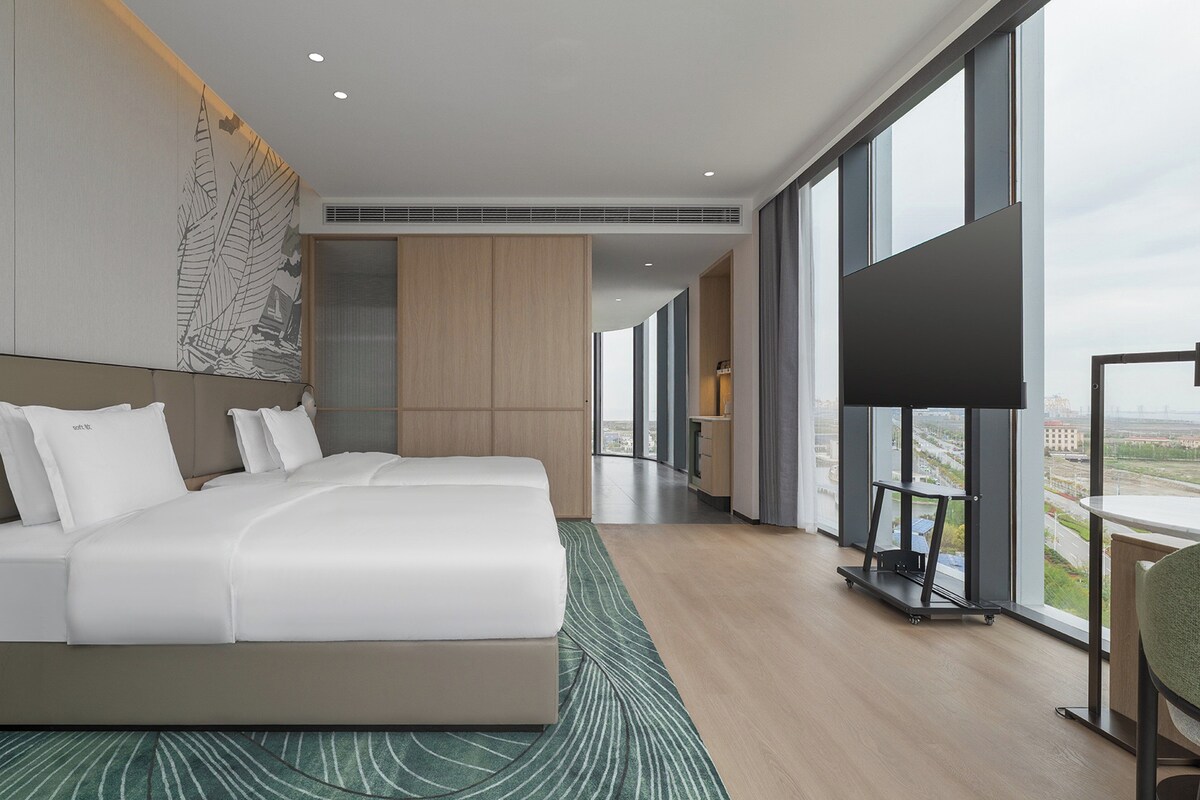 Quarto de hotel moderno com uma cama grande, uma TV e vista para a cidade.