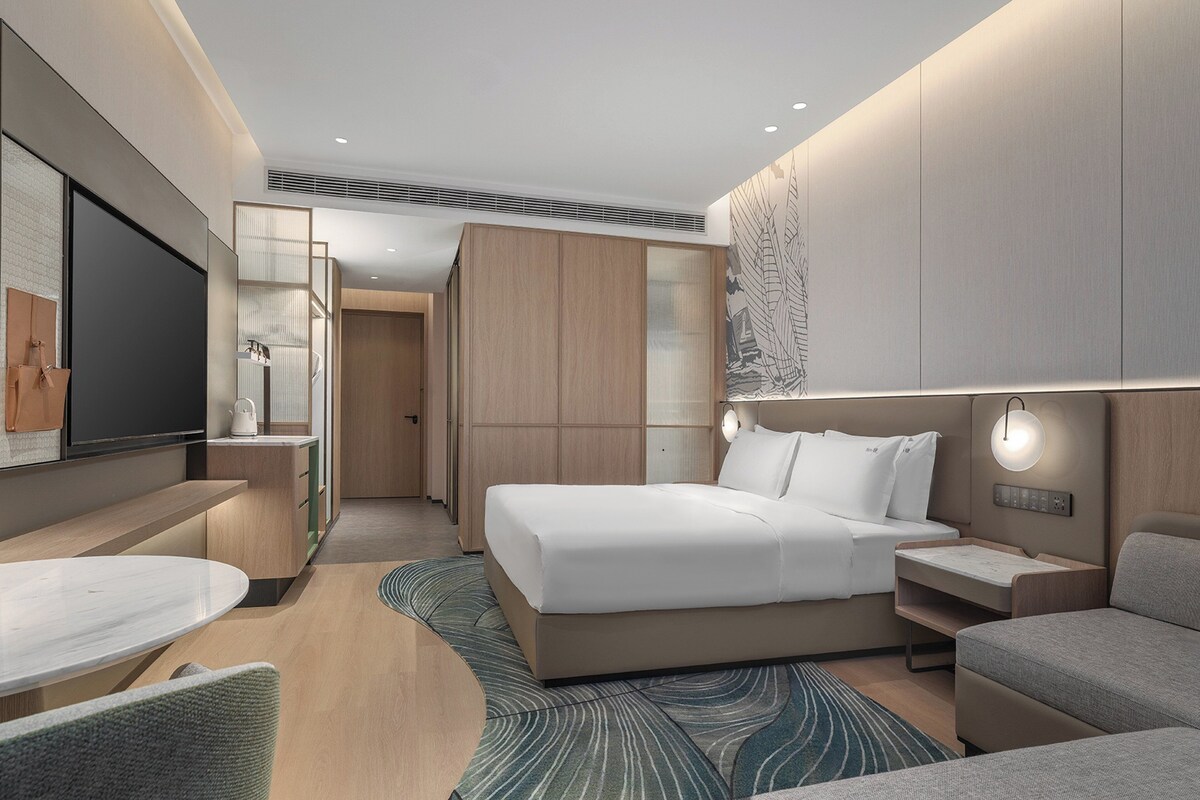 Quarto de hotel moderno com cama, mesas de cabeceira, TV de tela plana, escrivaninha e sofá.