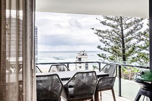 A balcony with a view of the ocean, a tree, and a building in the background. - Magnoli Bayview Escape (Palm Beach)