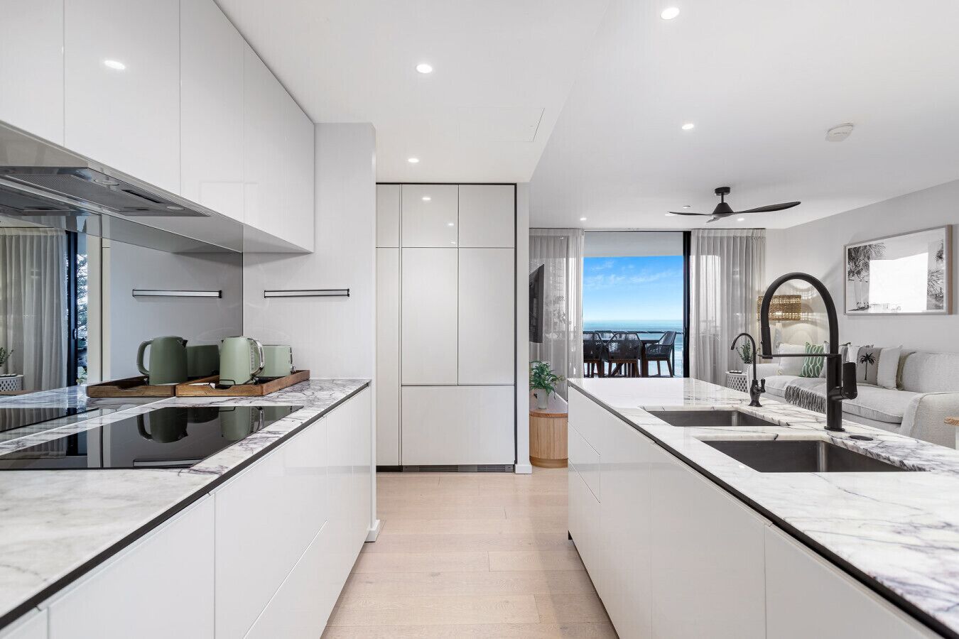 A modern kitchen with white cabinetry, a central island, and a view to a balcony.