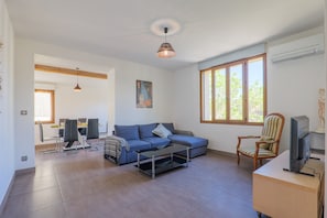 A living room with a sofa, coffee table, TV, and a dining area with chairs and a table. - Holiday Home in Southern Ardèche with Jacuzzi, Wi-Fi, and Air Conditioning (Joyeuse)