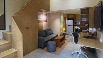 A modern interior with a staircase, a sofa, a desk, and a kitchen area.