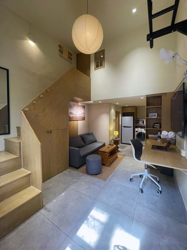 A modern interior with a staircase, a sofa, a desk, and a kitchen area.