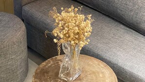 A grey sofa with a vase of dried flowers on a round wooden table.