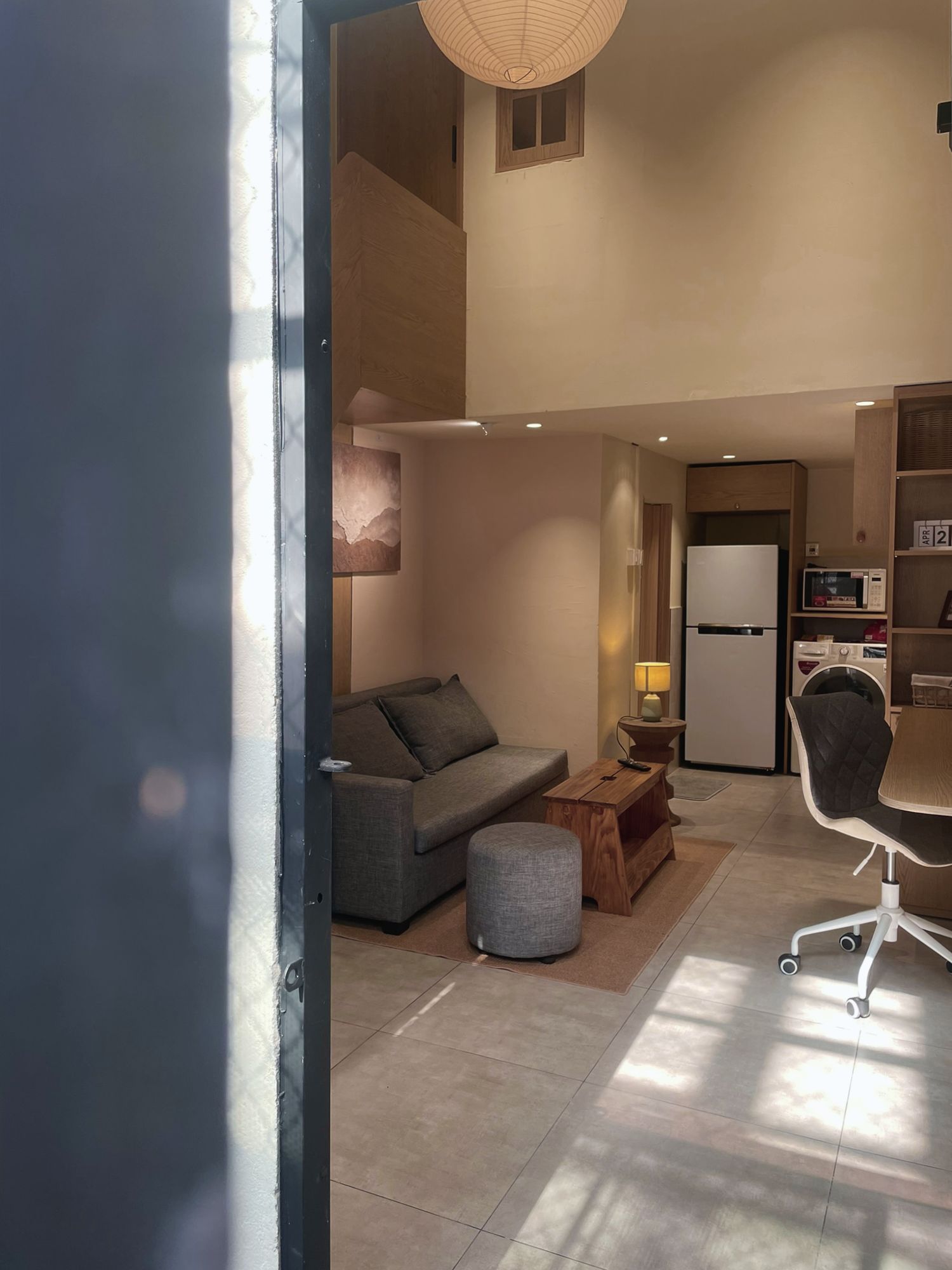 A modern living space with a sofa, ottoman, lamp, and a dining area with a chair and table.