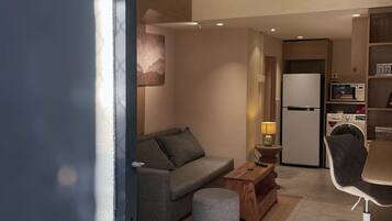 A modern living space with a sofa, ottoman, lamp, and a dining area with a chair and table.