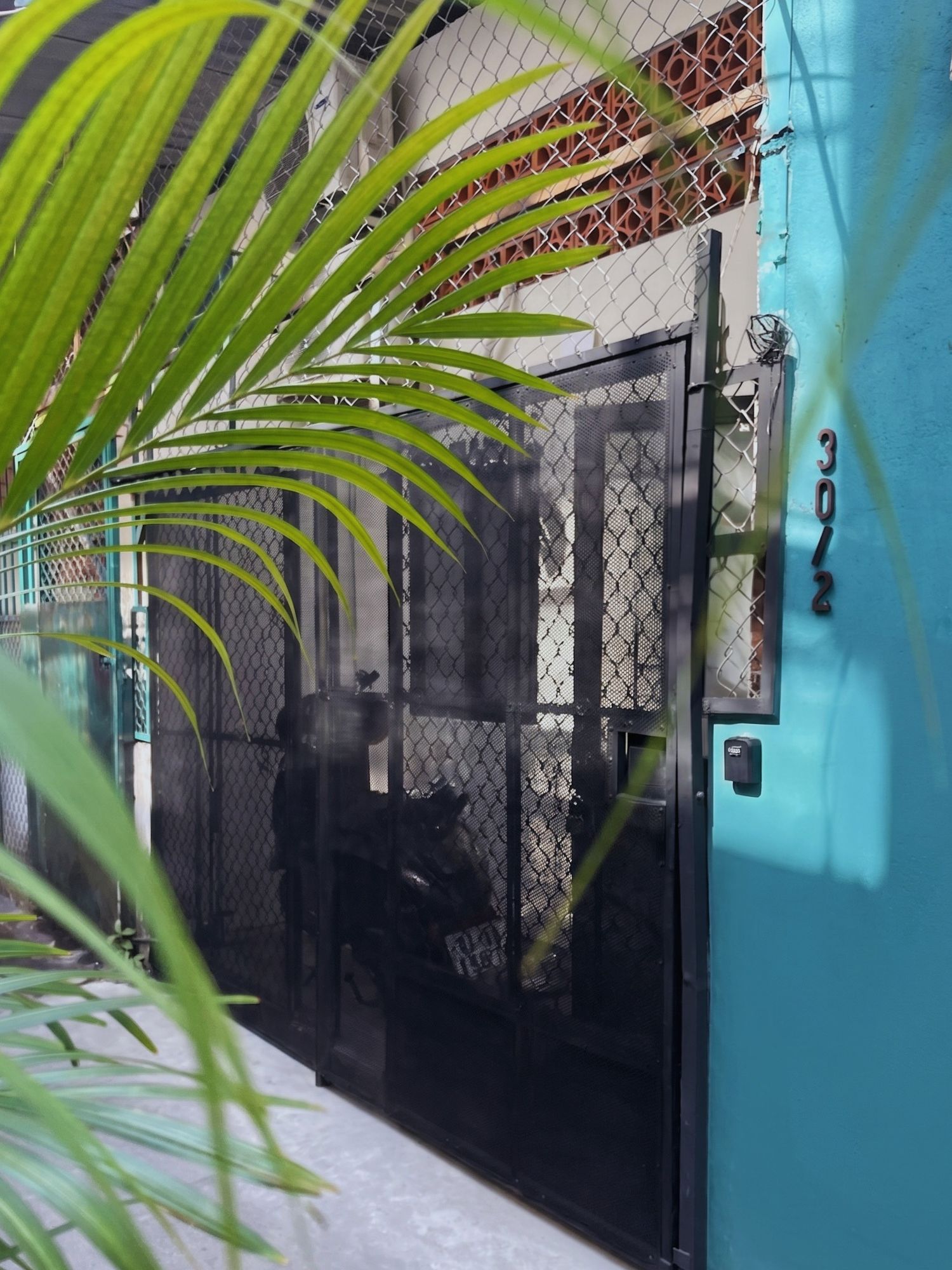A blue building with a mesh gate and a number '3012' on the wall.
