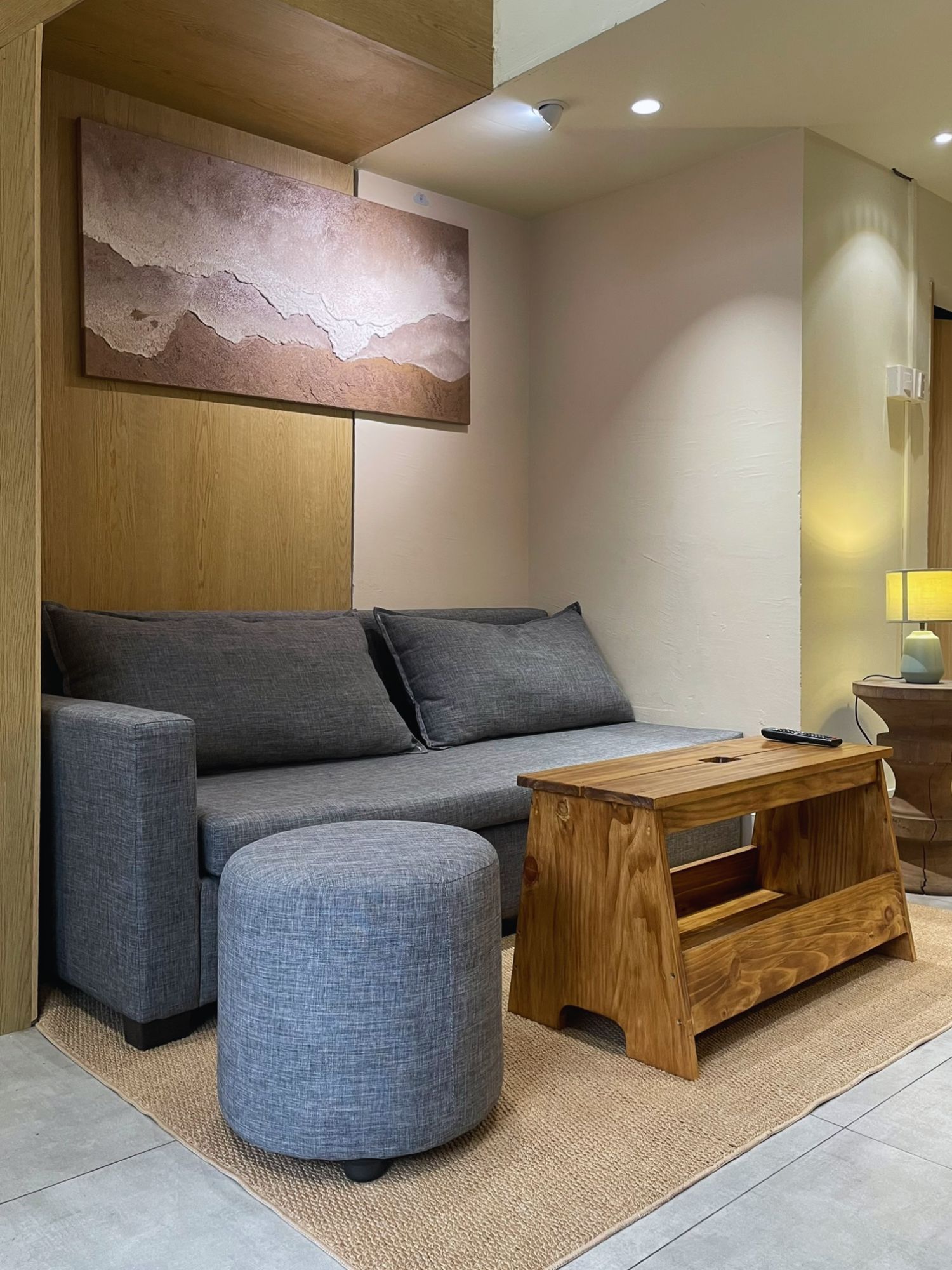 A modern living room with a grey sofa, a wooden coffee table, and a round ottoman.