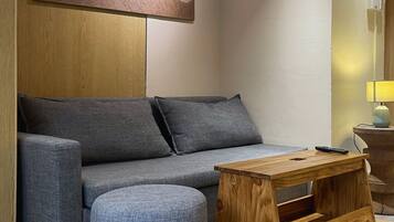 A modern living room with a grey sofa, a wooden coffee table, and a round ottoman.
