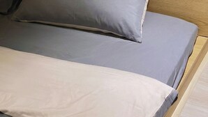 A bed with a grey and white mattress, a wooden headboard, and a white electrical outlet on the wall.