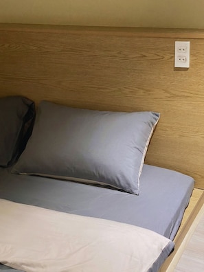 A bed with a grey and white mattress, a wooden headboard, and a white electrical outlet on the wall.