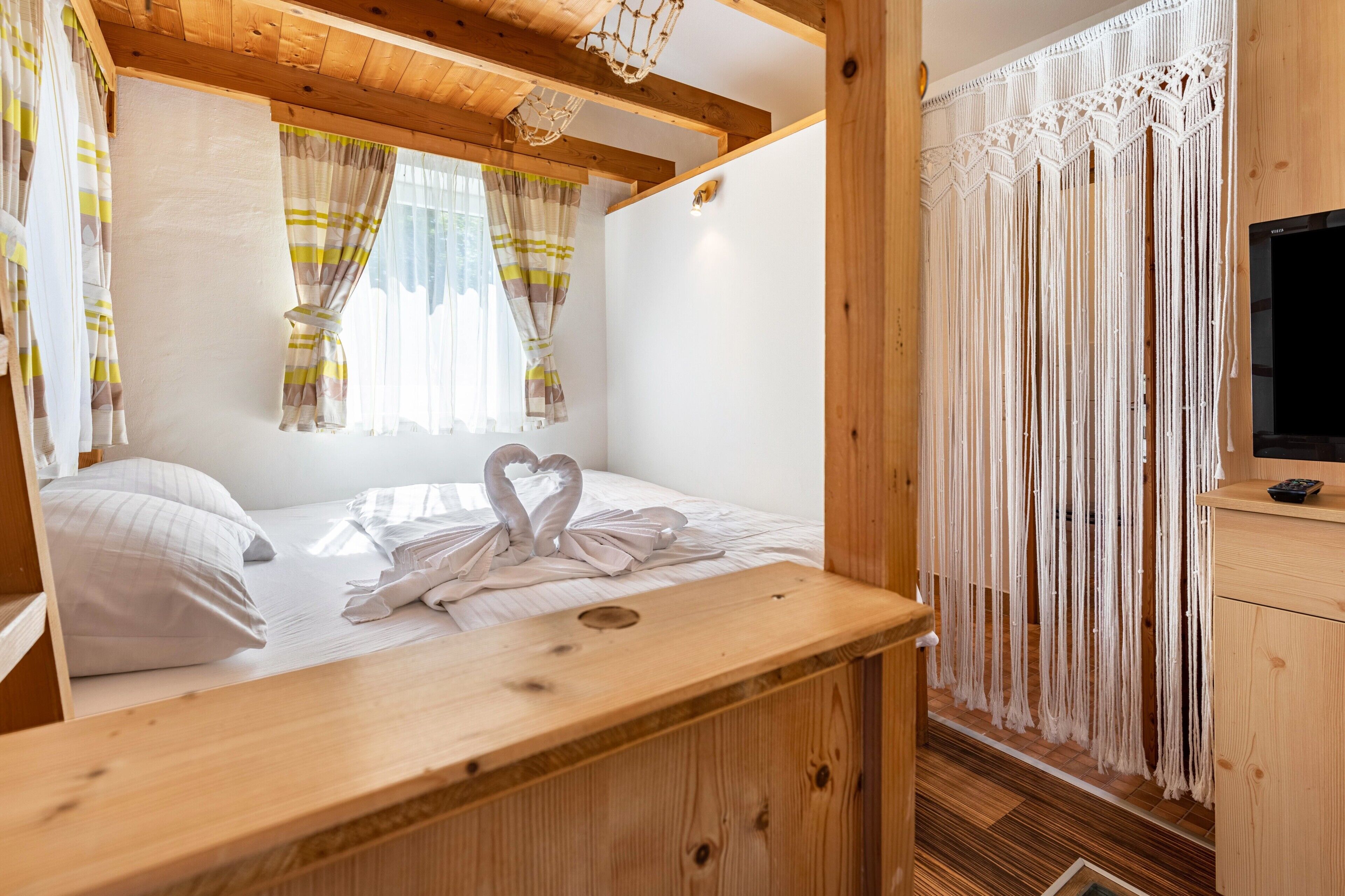 A cozy room with a wooden bed, a small desk, a TV, and a macrame curtain.