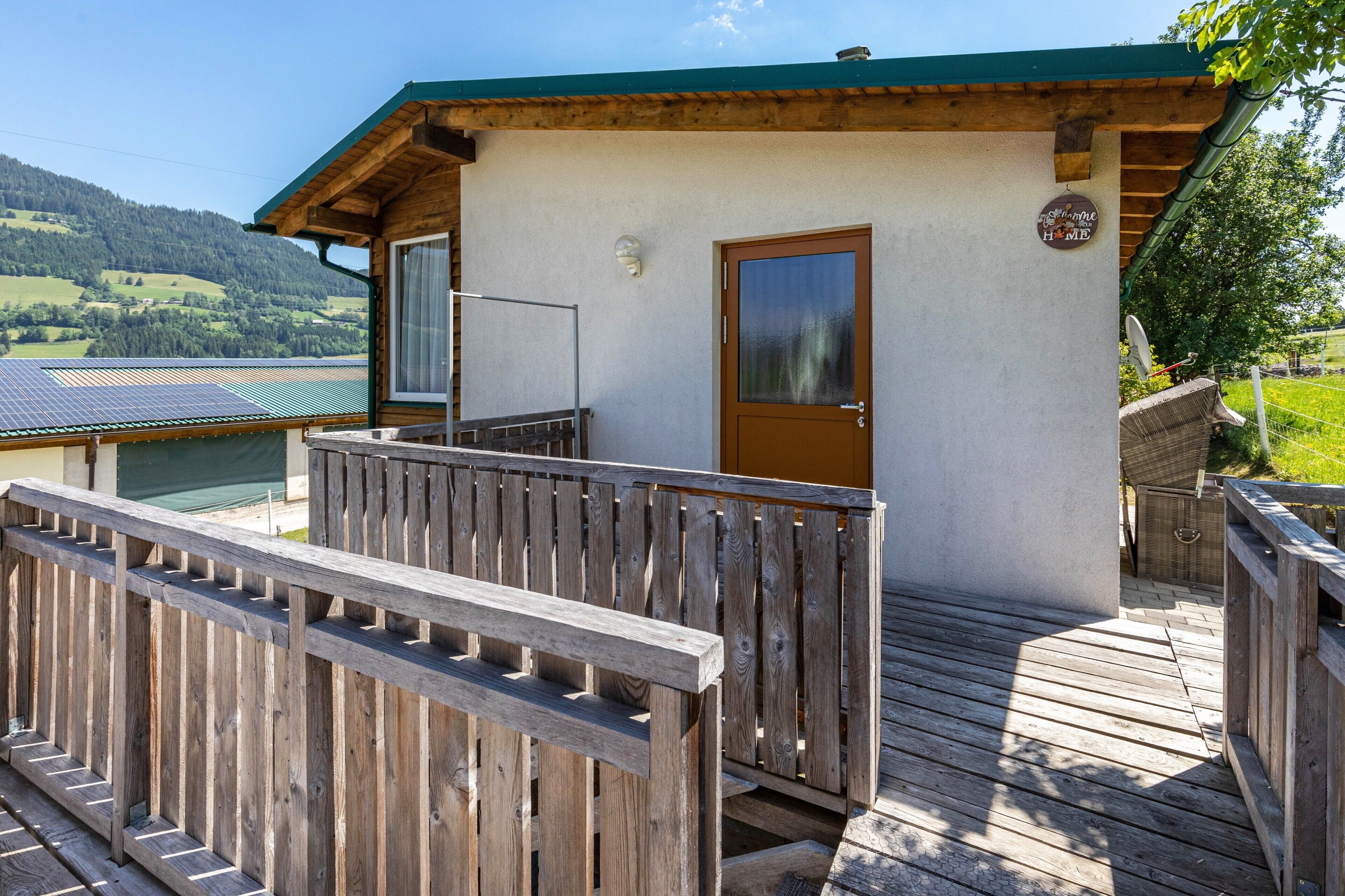 A wooden deck leading to a chalet with a door and a window, surrounded by a wooden fence.