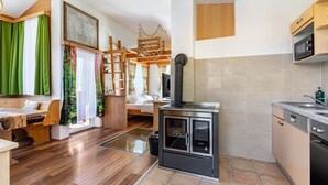 Uma cozinha moderna com uma lareira a lenha, uma área de jantar com bancos e vista para um quarto com cama e cortinas.