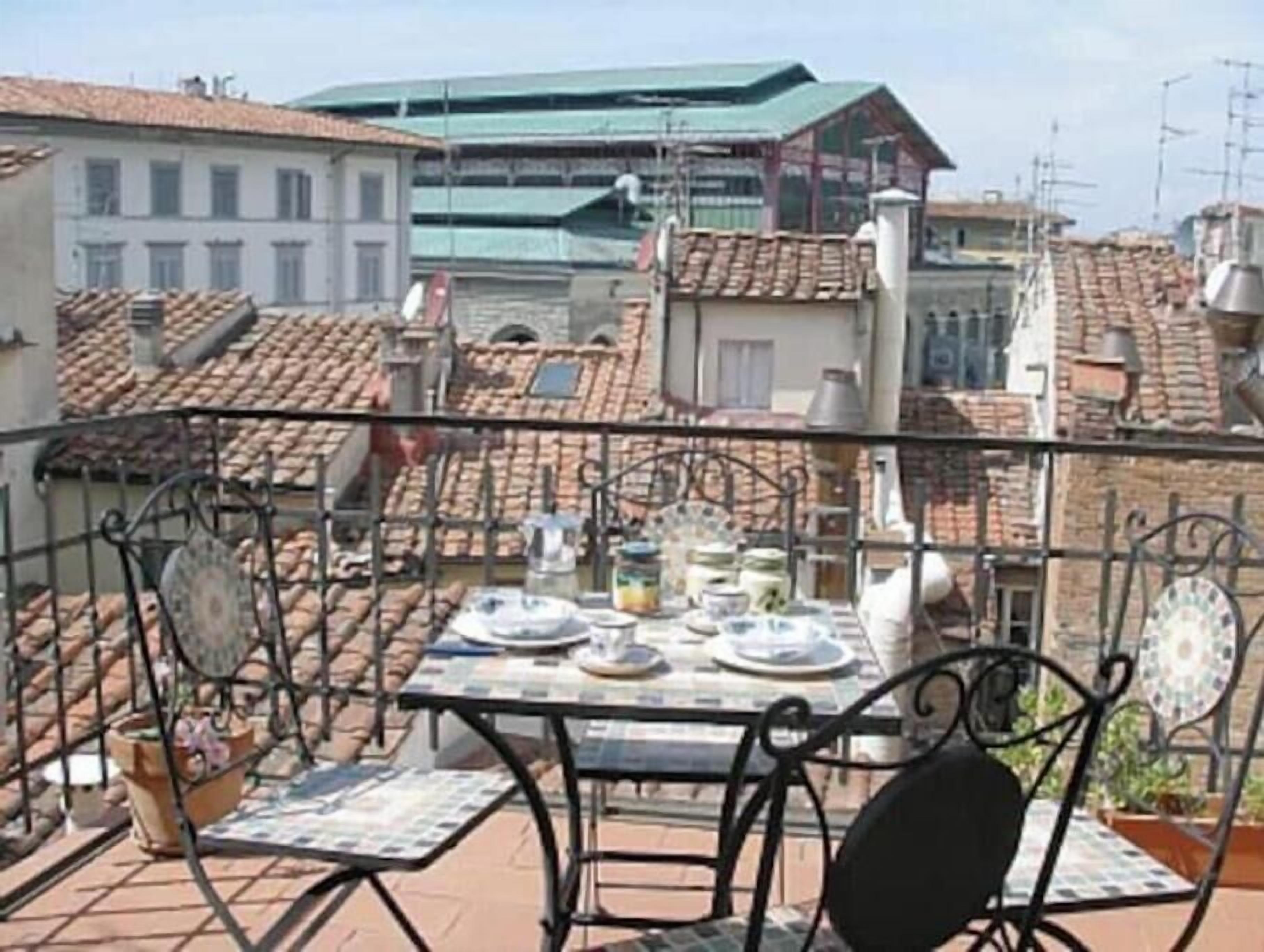 Un balcone con un tavolo apparecchiato per mangiare, circondato da ringhiere in metallo e piante in vaso.