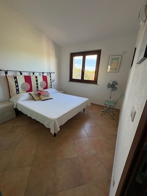 Une chambre à coucher avec un lit, une fenêtre, un ventilateur et une chaise.