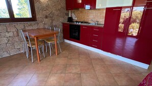 A kitchen with a stone wall, red cabinets, a wooden dining table, and a window. - Holiday Home 'Appartamento Baia 12' with Private Garden, Wi-Fi and Air Conditioning (Baia Vignola)