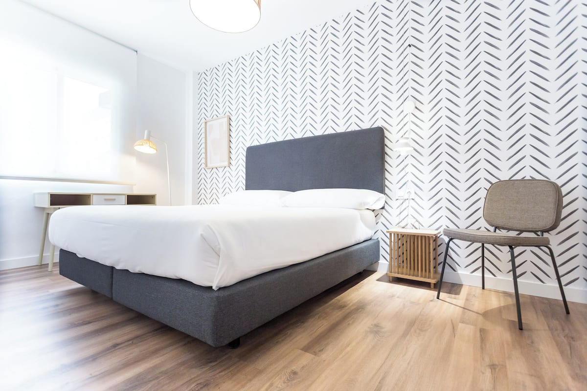 A modern bedroom with a bed, a desk, a chair, and a radiator.