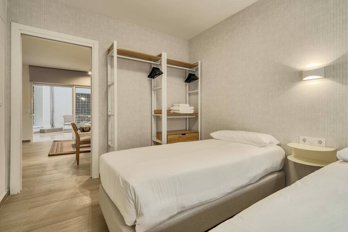 A hotel room with two beds, a wardrobe, a bedside table, and a view of the outside.