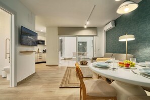A modern kitchen with a flat-screen TV, a dining area with a table set for two, and a view into the living area. - MOON Apartments (Seville)