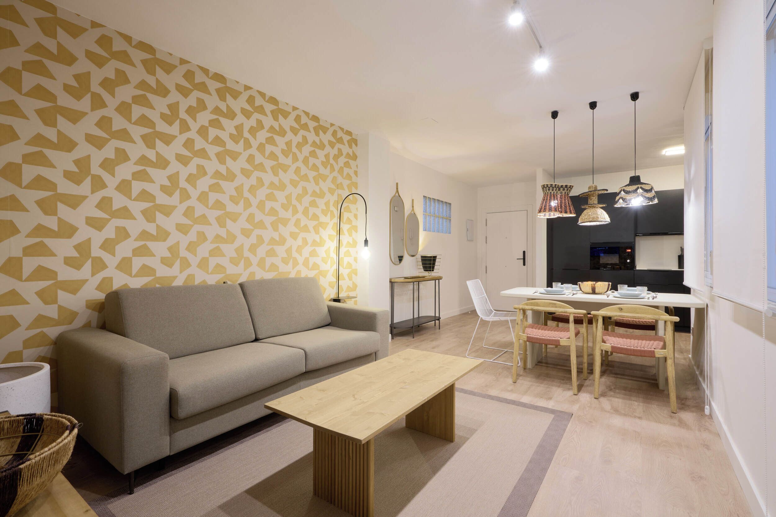 A modern living room with a sofa, a wooden coffee table, a dining area with a table and chairs, and a kitchen in the background.