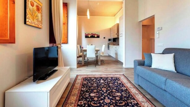 Un soggiorno moderno con una TV a schermo piatto, un divano, un tappeto decorato e, sullo sfondo, una zona pranzo.