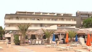 A hotel with multiple balconies, outdoor seating with umbrellas, and a sandy beach area.