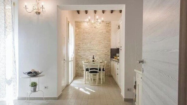 A hallway leading to a dining area with a stone wall, a chandelier, and a small table with a bowl of fruit. - Little Box House - Modern design and tranquility in the heart of the city (Firenze)