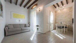 A modern living room with a sofa, a dining table with chairs, a chandelier, and a stone wall. - Little Box House - Modern design and tranquility in the heart of the city (Firenze)