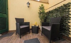 Eine Sitzecke mit zwei Korbstühlen, einem kleinen runden Tisch, einem Blumentopf und einer Wandleuchte.