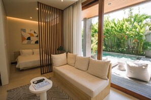 A modern bedroom with a sofa, a bed, a small table, and a view of a pool. - TheHub Pererenan (Canggu)