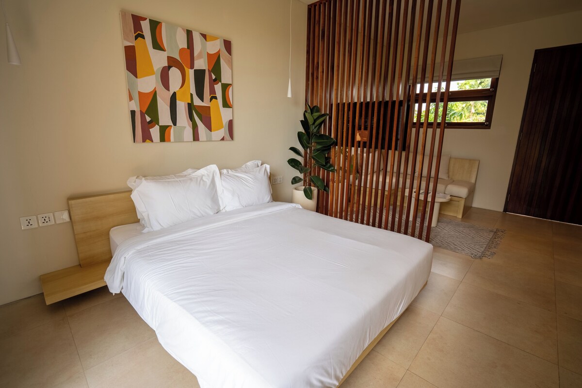 Quarto moderno com uma cama grande, cabeceira de madeira, uma planta em vaso e uma janela com vista.