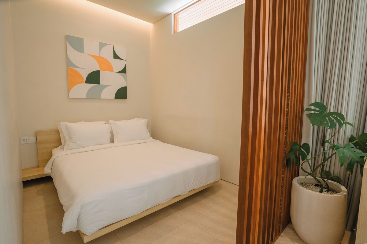 Quarto moderno com cama, um quadro abstrato na parede, planta em vaso e janela com persianas.