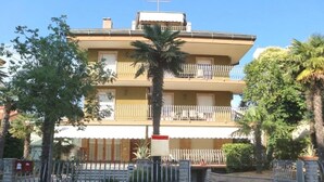 Un edificio de varios pisos con balcones, una palmera y una entrada portonada.