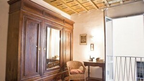 A room with a large wooden wardrobe, a wicker chair, a small table, and a balcony with a railing. - An authentic stay in the heart of Florence, a stone's throw from history (Firenze)