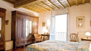 A bedroom with a wooden wardrobe, a bed with a floral bedspread, a chair, a small table, and a window with a view. - An authentic stay in the heart of Florence, a stone's throw from history (Firenze)