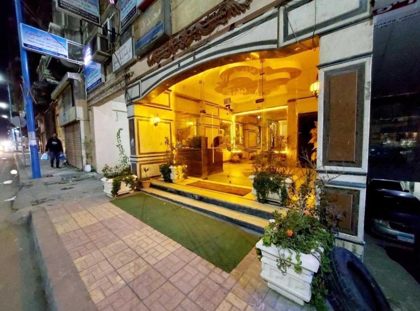 A hotel entrance with a welcoming archway, a small outdoor pool, and potted plants.