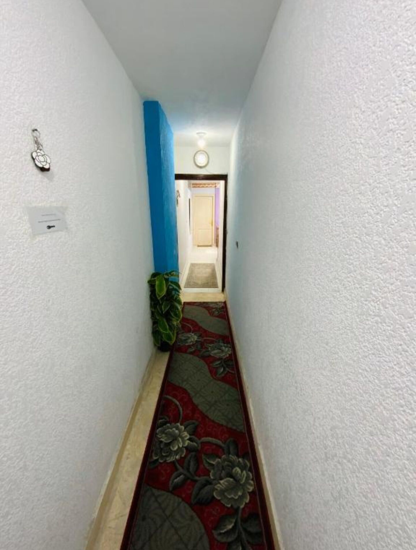 A narrow hallway with a red carpet, a blue wall, and a door at the end.
