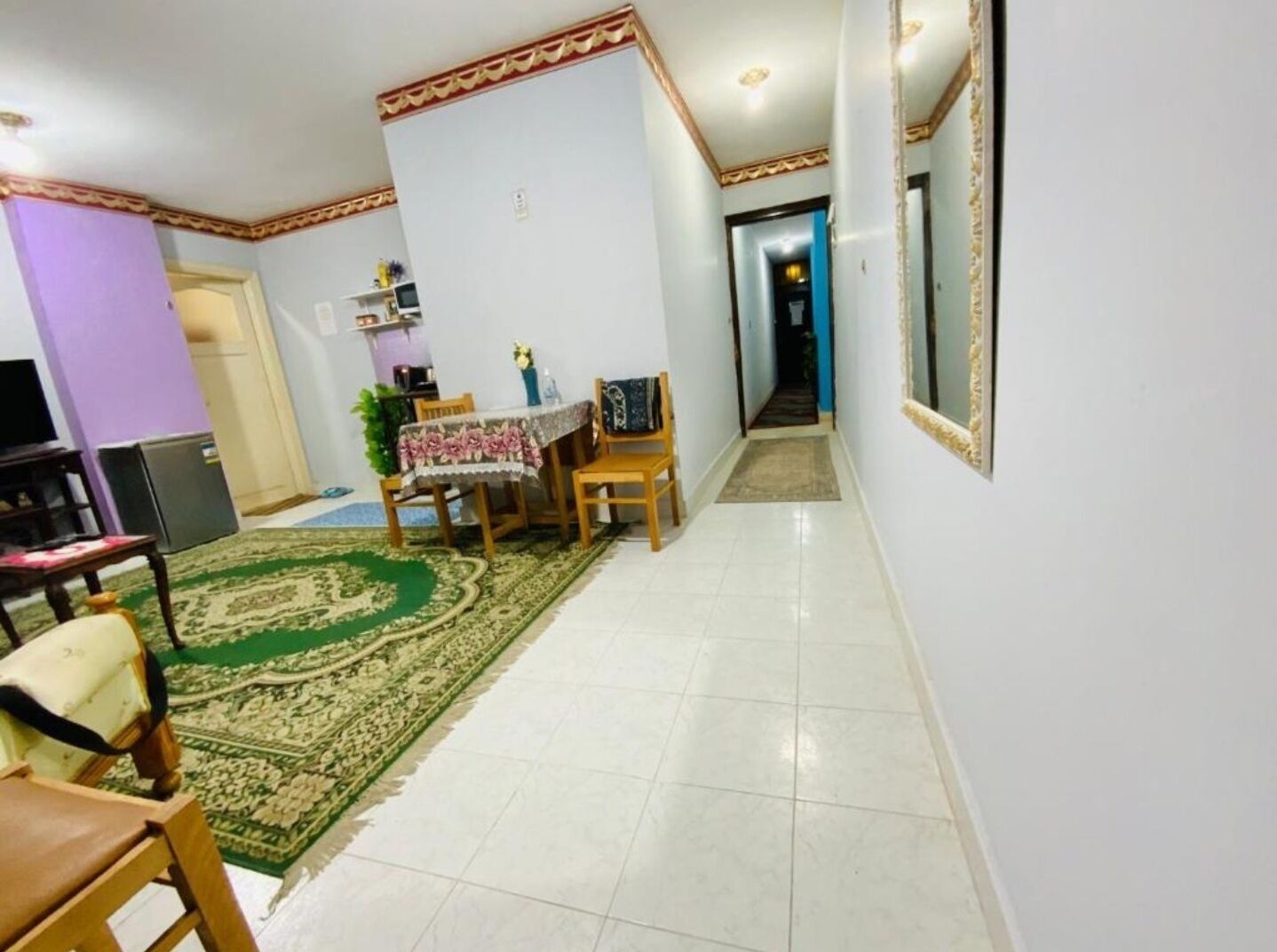 A dining area with a table set for two, a patterned rug, and a hallway leading to another room.