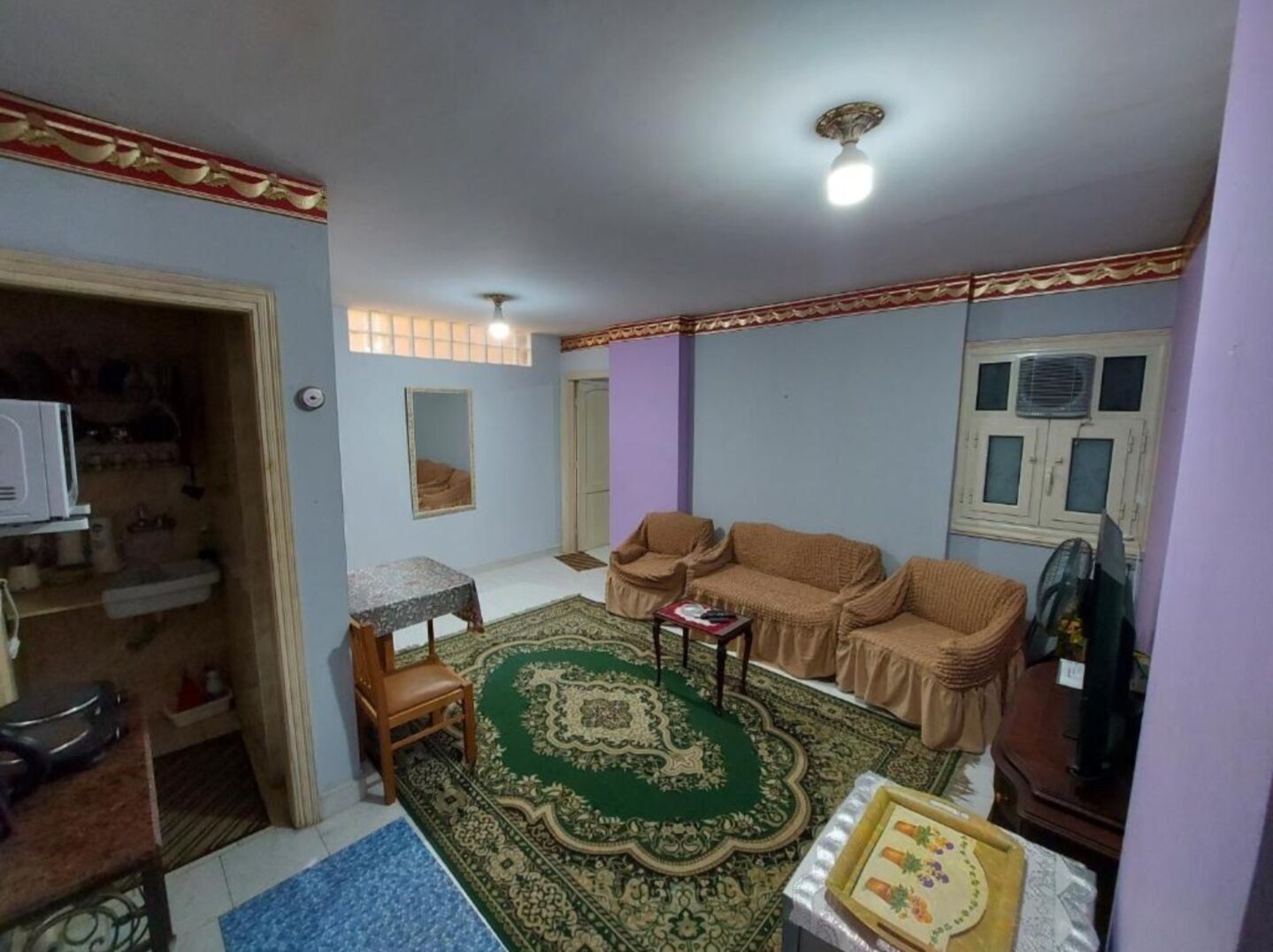 A living room with a sofa set, a coffee table, a patterned rug, a small table with a chair, and a television.